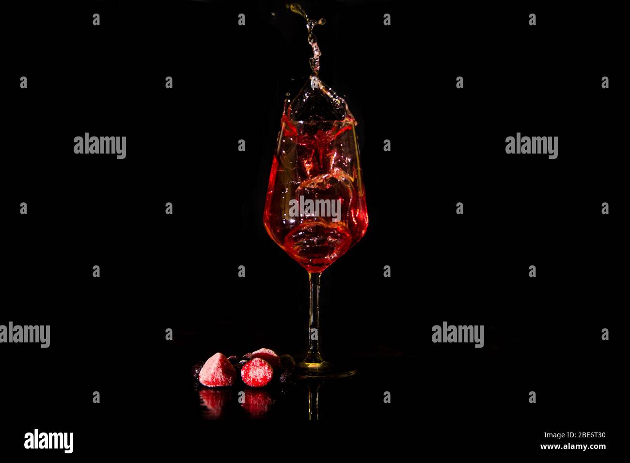 vino rosso o rosa che si spruzzi da un bicchiere di vino su uno sfondo nero con bacche. Tasto basso di splash del vino Foto Stock