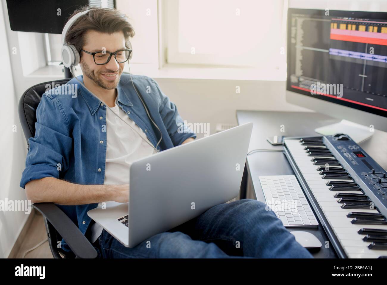 Lavorare su un notebook. Ragazzo occupato. Concetto di multitasking. DJ in studio di trasmissione. Produttore di musica sta componendo una canzone su tastiera sintetizzatore e. Foto Stock