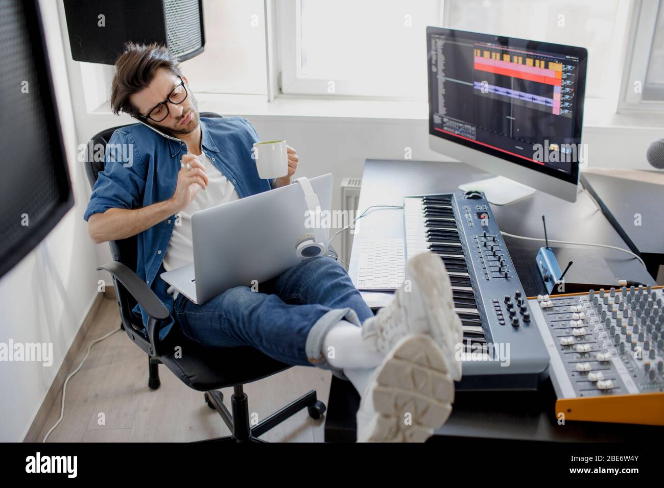 Parlare al telefono e lavorare su un computer portatile. Ragazzo occupato. Concetto di multitasking. DJ in studio di trasmissione. Produttore di musica sta componendo una canzone su Foto Stock