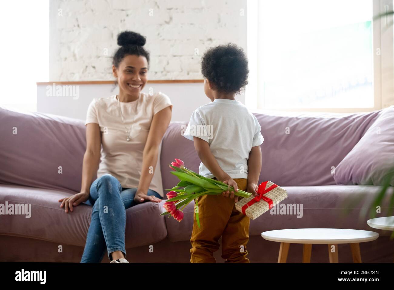 Vista posteriore african american figlio che tiene fiori, bouquet e regalo. Foto Stock