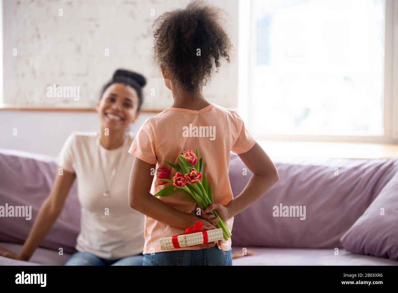 Vista posteriore figlia african american che tiene fiori, bouquet e regalo. Foto Stock