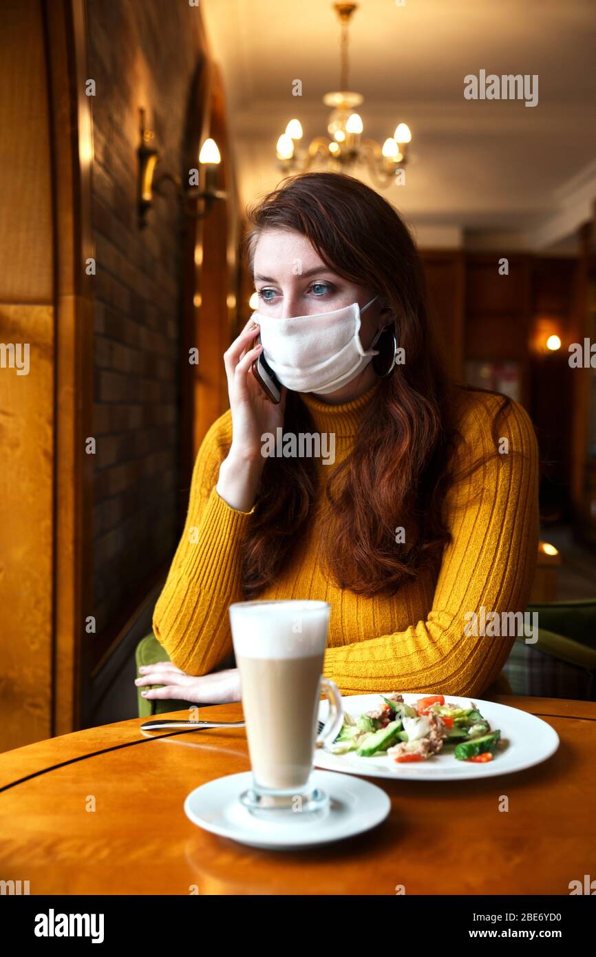 Giovane ragazza che indossa una maschera protettiva che parla al telefono in caffetteria Foto Stock