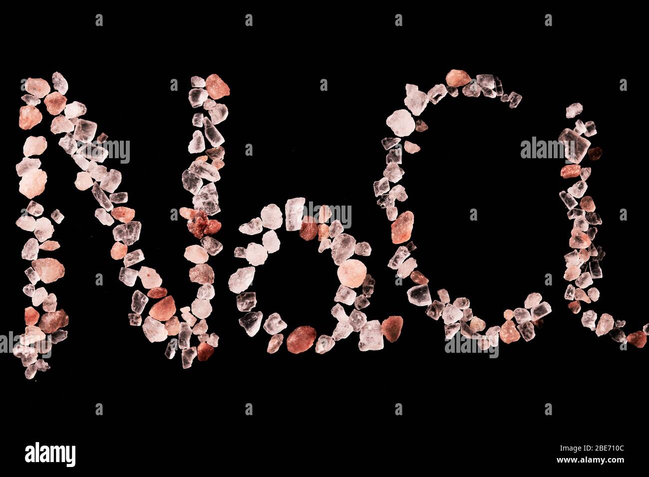 Macro fotografia del sale di Himalaya con il simbolo chimico NaCl scritto isolato su sfondo nero. Concetto di benessere e benessere, mangiare e cucinare Foto Stock