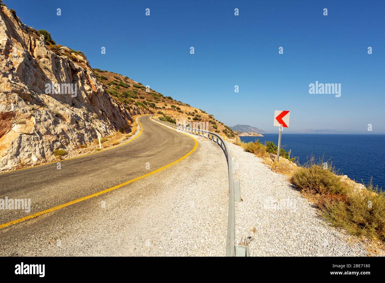 Curva strada asfaltata mediterranea e cartello curva in una calda giornata di sole. Datca, Turchia. Foto Stock