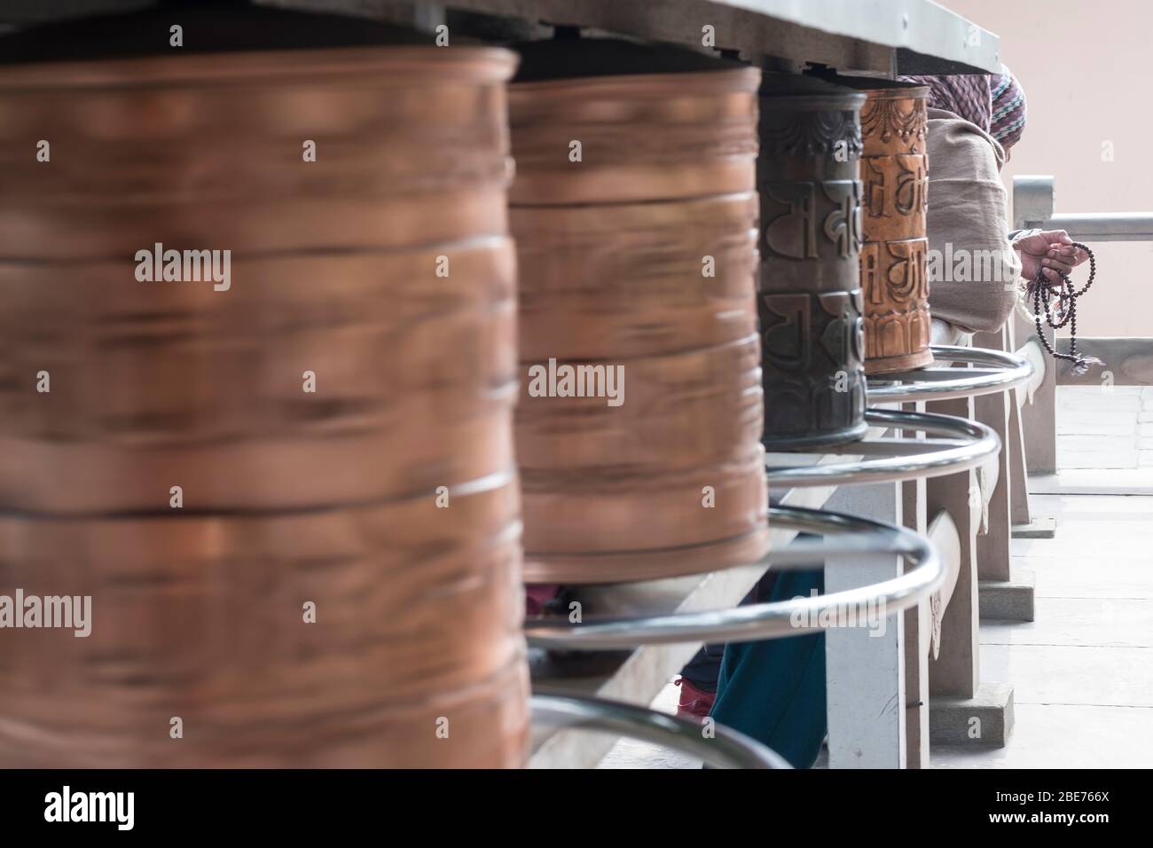 Ruota di preghiera in un tempio buddista a Varanasi con una vecchia signora che prega con le perle di preghiera Foto Stock