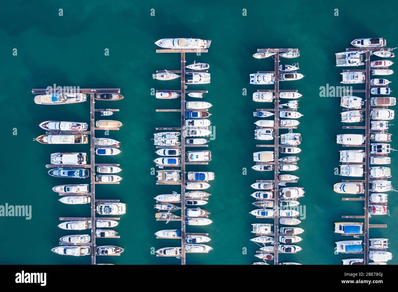 Vista aerea di un yacht a motore bianco. Lo yacht entra nella baia nel parcheggio. Molti yacht diversi, catamarani ormeggiati ai moli. Yacht e tr costosi Foto Stock