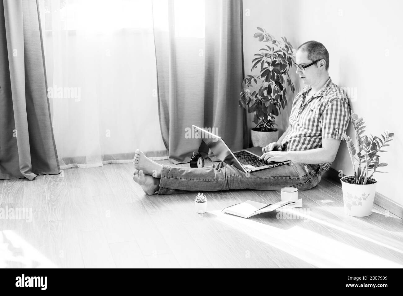 Giovane uomo sta lavorando a casa su un computer con telefono e una tazza di caffè monocromatico. Lavoro remoto, lavoro da casa. Foto Stock
