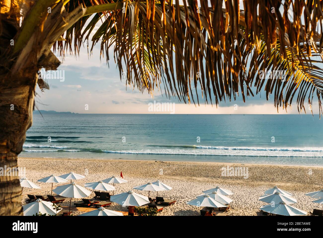 Bella alba, tramonto del sole attraverso le nuvole, i raggi del sole attraverso le nuvole, spiaggia sabbiosa con piccole onde, calda luce del mattino i Foto Stock