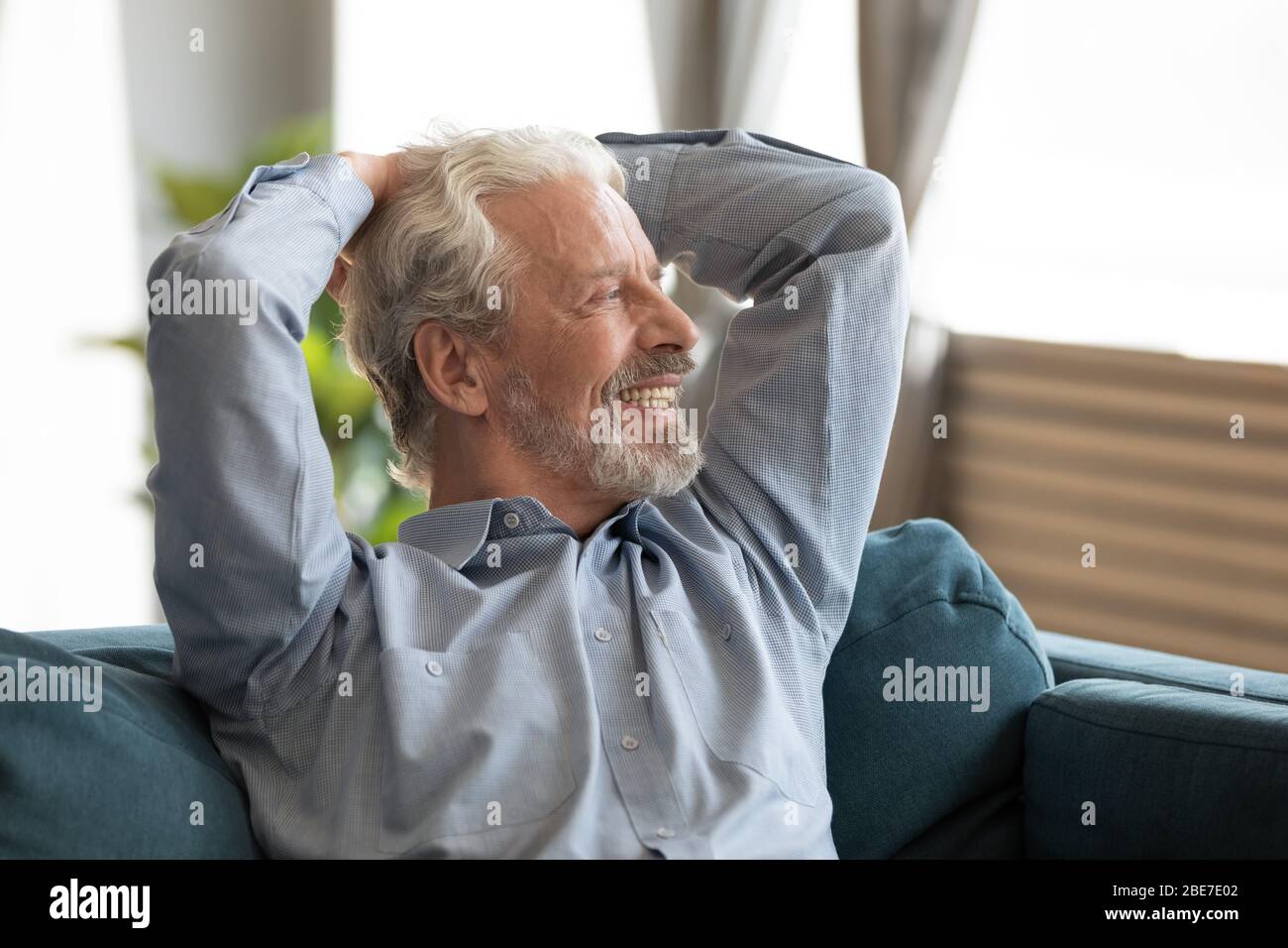 Uomo anziano sorridente che si rilassa sul divano, sogna, guardando lontano Foto Stock