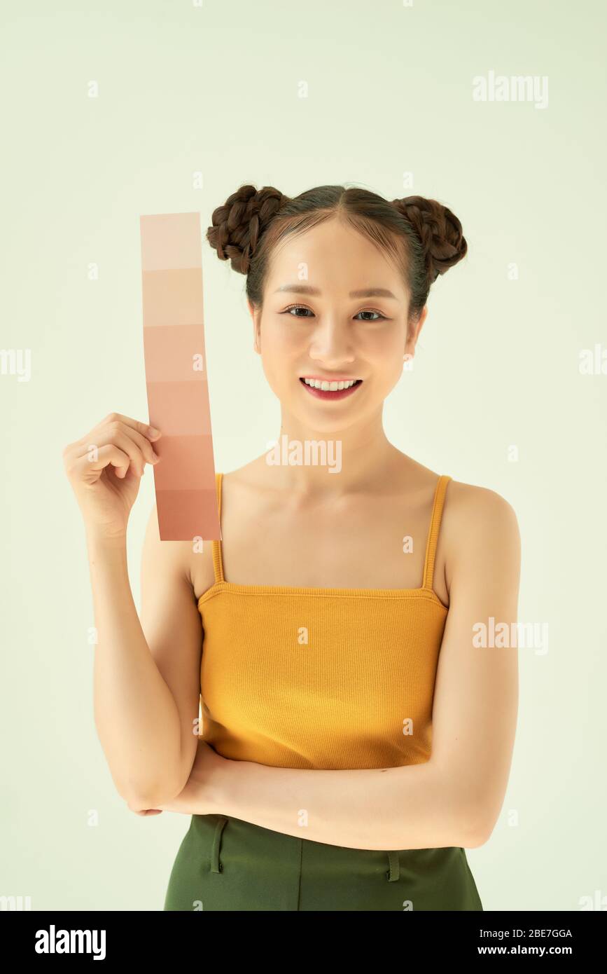 Giovane donna sorridente con tavolozza dei toni della pelle o campioni mentre si levano in piedi su sfondo chiaro Foto Stock