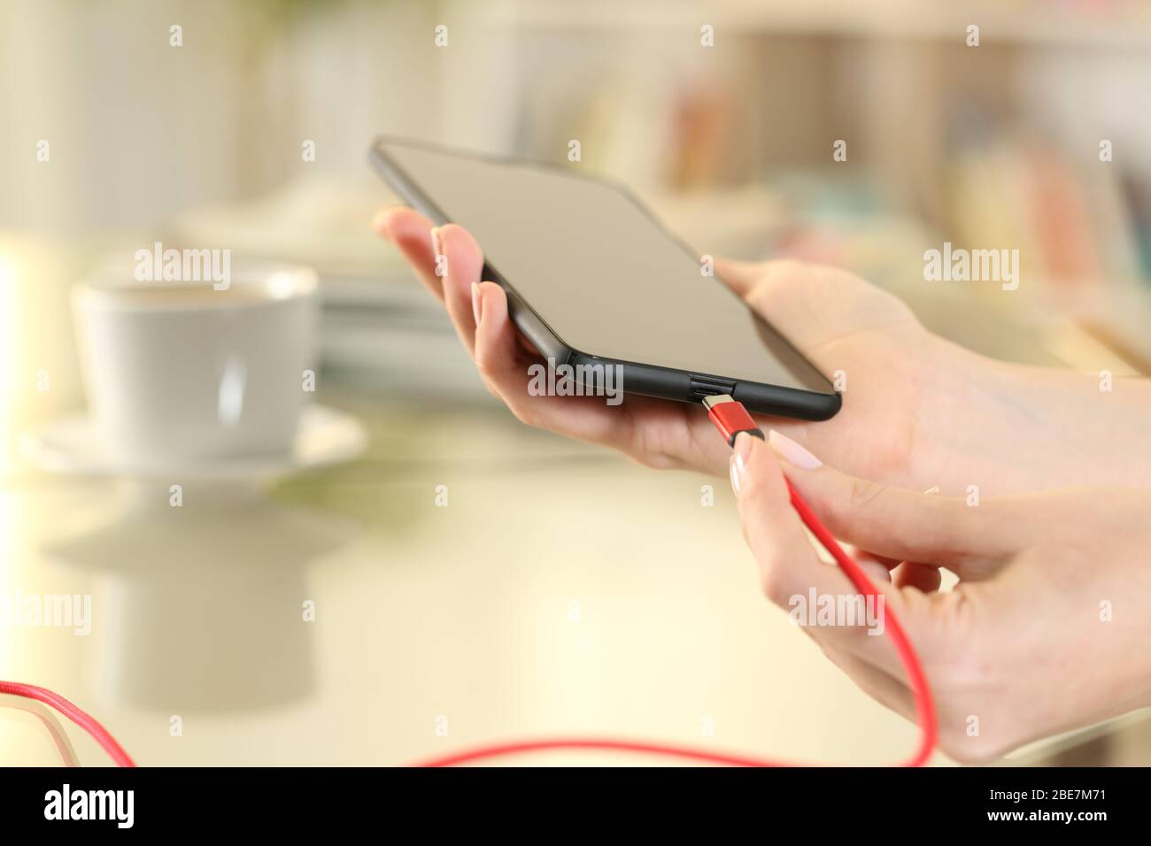 Primo piano di una donna che collega il cavo del caricabatterie usb c sullo smartphone seduto su una scrivania a casa Foto Stock