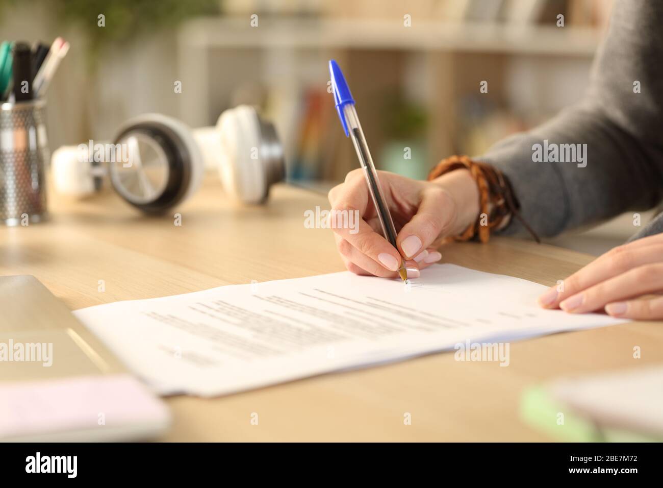 Primo piano delle mani della ragazza della studentessa firma del documento contrattuale che si trova su una scrivania a casa Foto Stock
