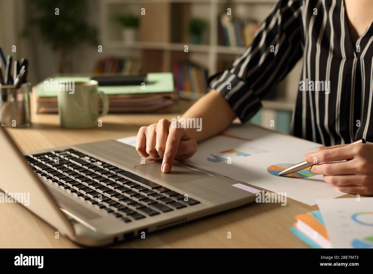 Primo piano delle mani dell'imprenditore confrontando il rapporto grafico di notte sul laptop a casa Foto Stock