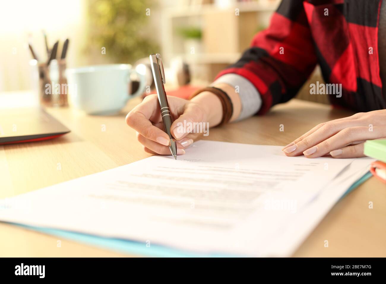 Primo piano di mani studentesca firma contratto su una scrivania a casa Foto Stock