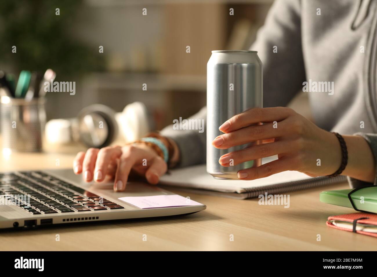 Primo piano di mani studentesse ragazza che tiene energia bevanda può di notte studiare su una scrivania a casa Foto Stock