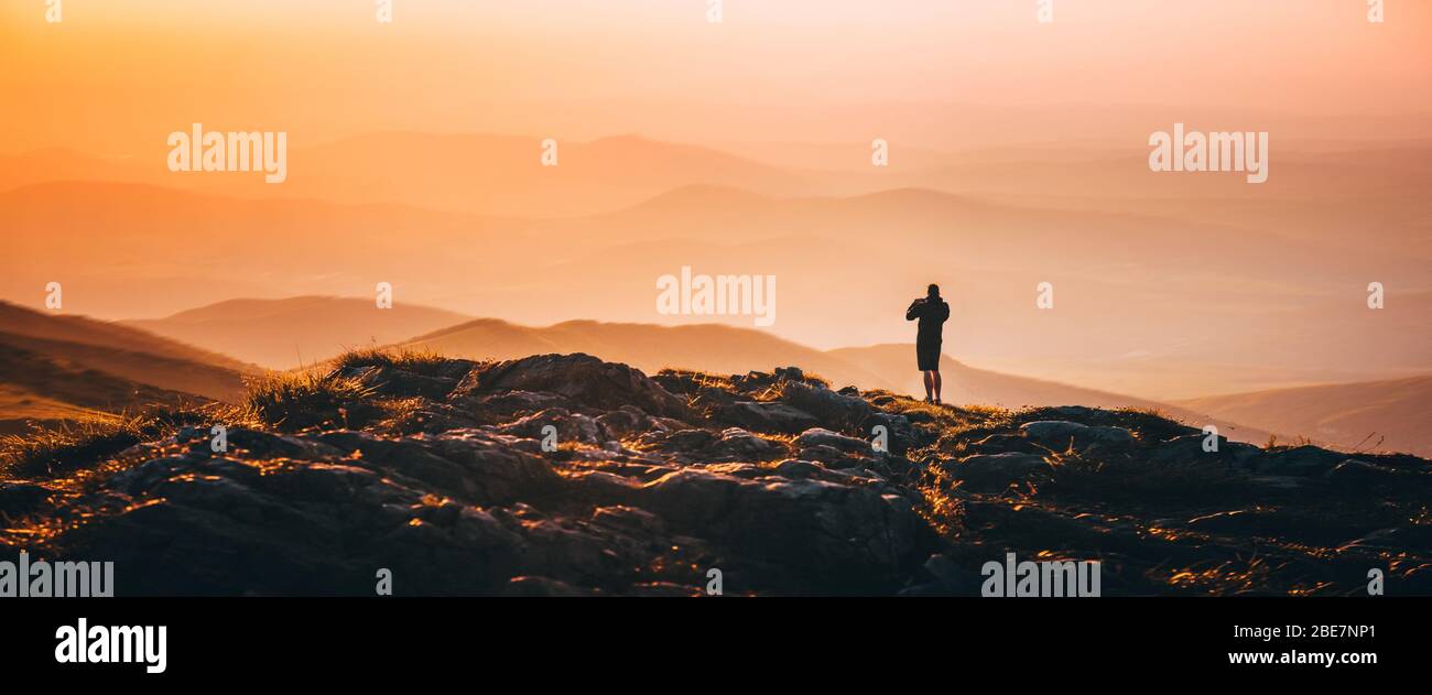 Banner, pagina web o copertina di un solo uomo in piedi sulla cima della collina sul prato delle montagne con un bellissimo tramonto colorato sul paesaggio. Foto Stock