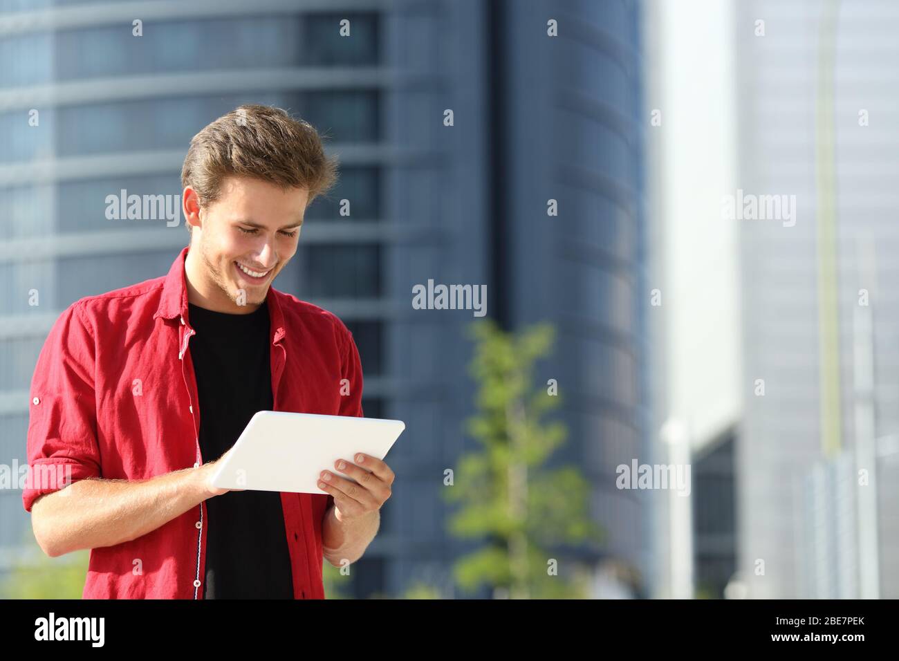 Un uomo felice che si trova in strada utilizzando un tablet in una zona commerciale della città Foto Stock