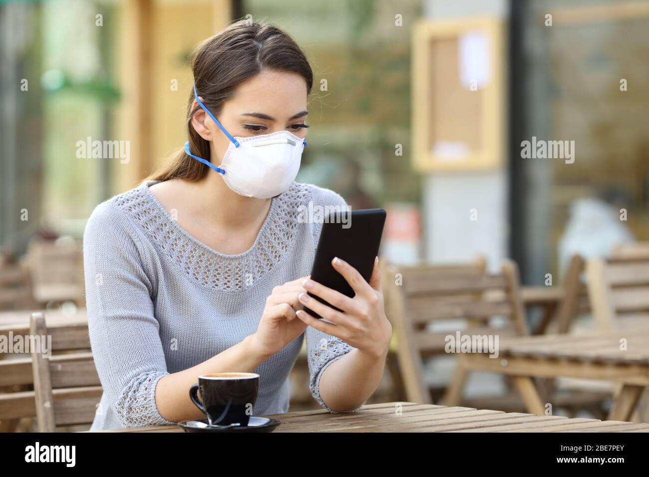 Donna seria con maschera protettiva evitando contagio controllare notizie su smartphone in un bar Foto Stock