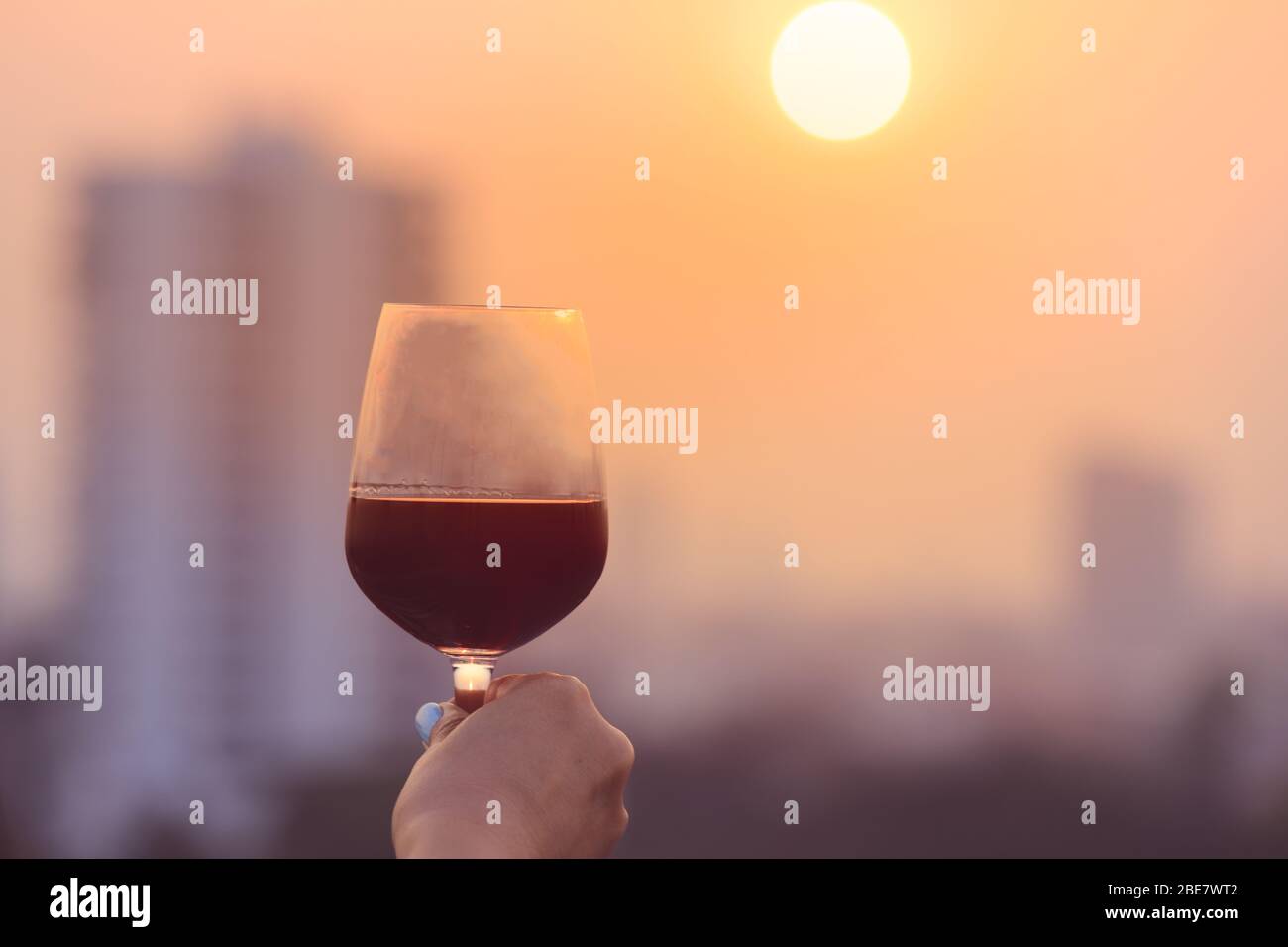 Mano della donna che tiene i bicchieri di vino rosso sul balcone durante il tramonto, concetto di festa Foto Stock