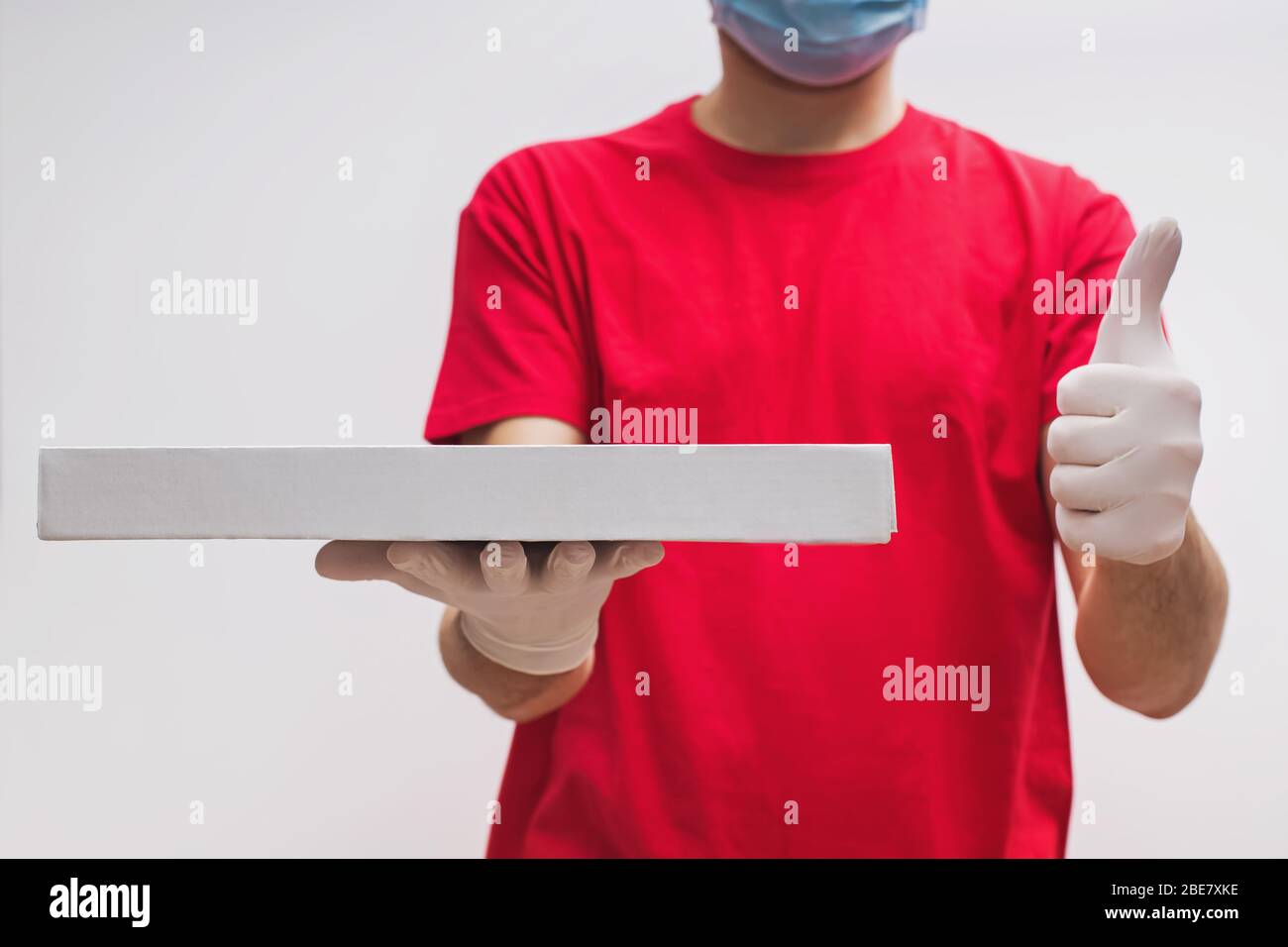 Uomo dal servizio di consegna in t-shirt rossa, indossando maschera protettiva e guanti che tengono la scatola della pizza Foto Stock