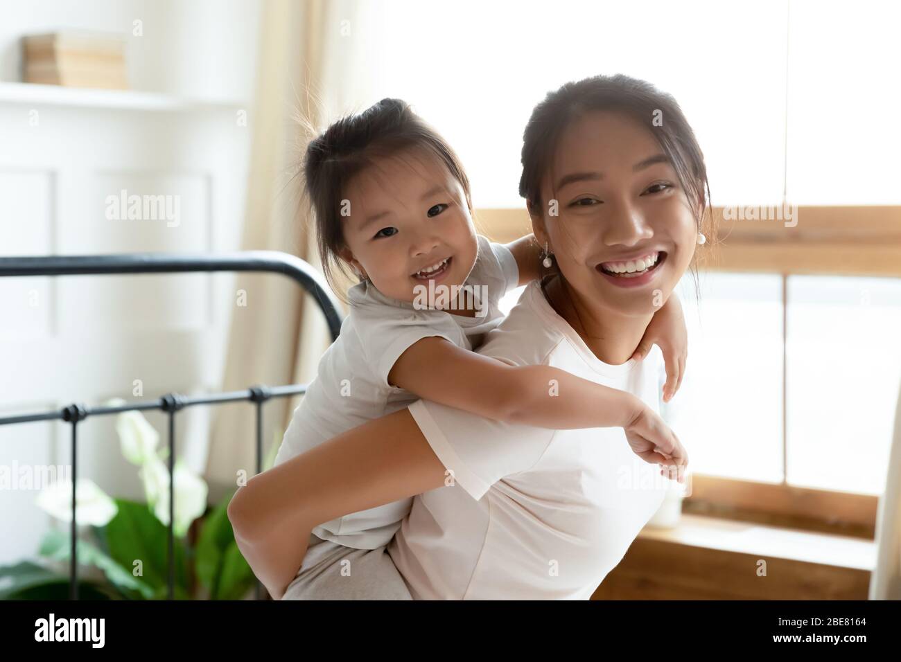 Piccola adorabile figlia piggybacks sua giovane madre asiatica Foto Stock
