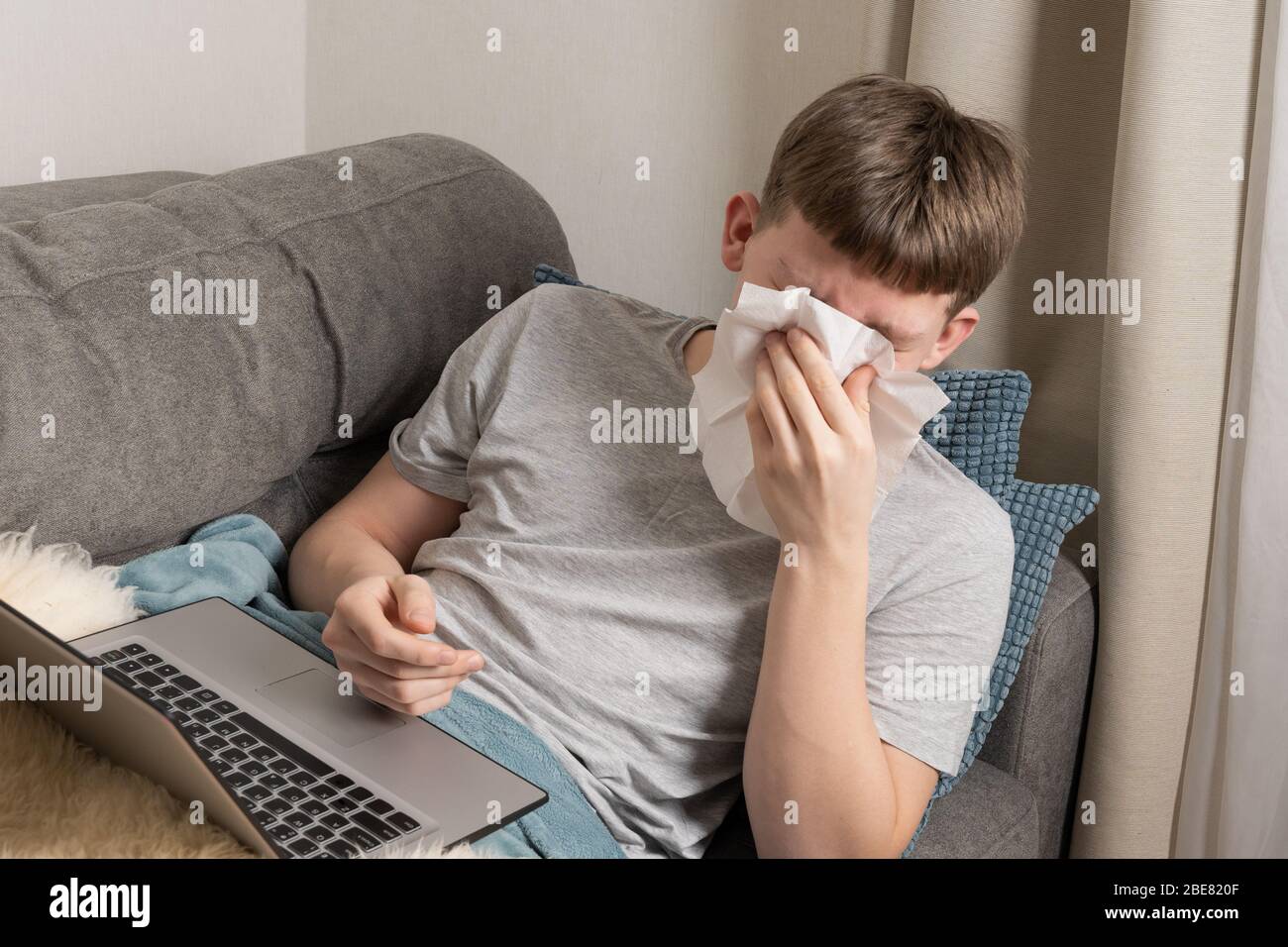 Un adolescente malato cerca di studiare online e starnutisce in un asciugamano di carta. Autoisolamento. Quarantena. elearning a distanza. Prevenzione di Coronavirus. Foto Stock