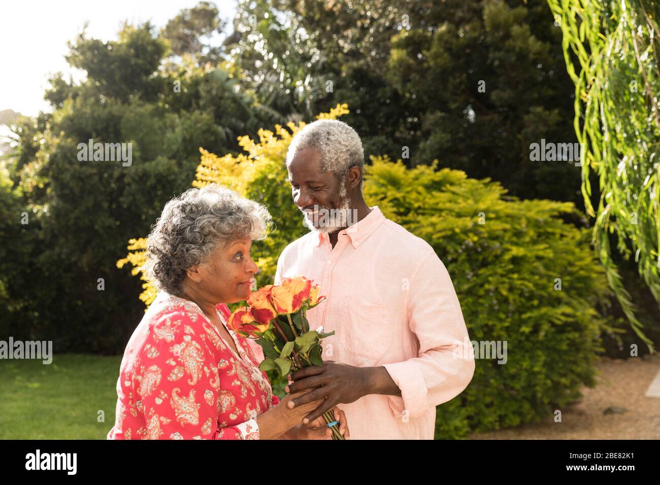 Un uomo afro-americano che offre fiori alla moglie, trascorrendo insieme del tempo in giardino Foto Stock