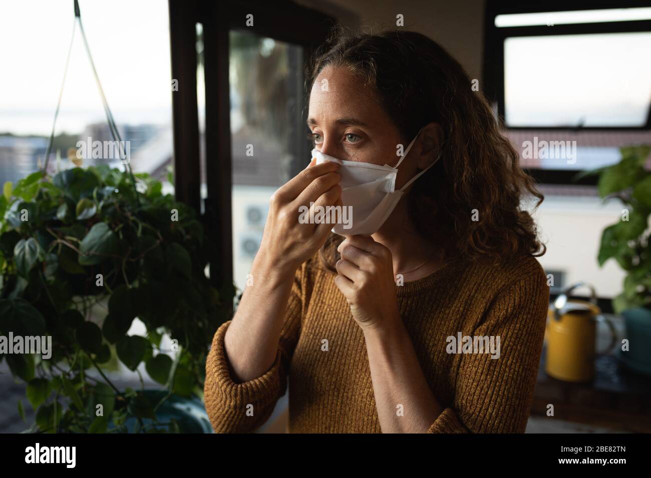 Donna che indossa una maschera facciale a casa. Distanza sociale in quarantena durante l'epidemia di coronavirus Foto Stock