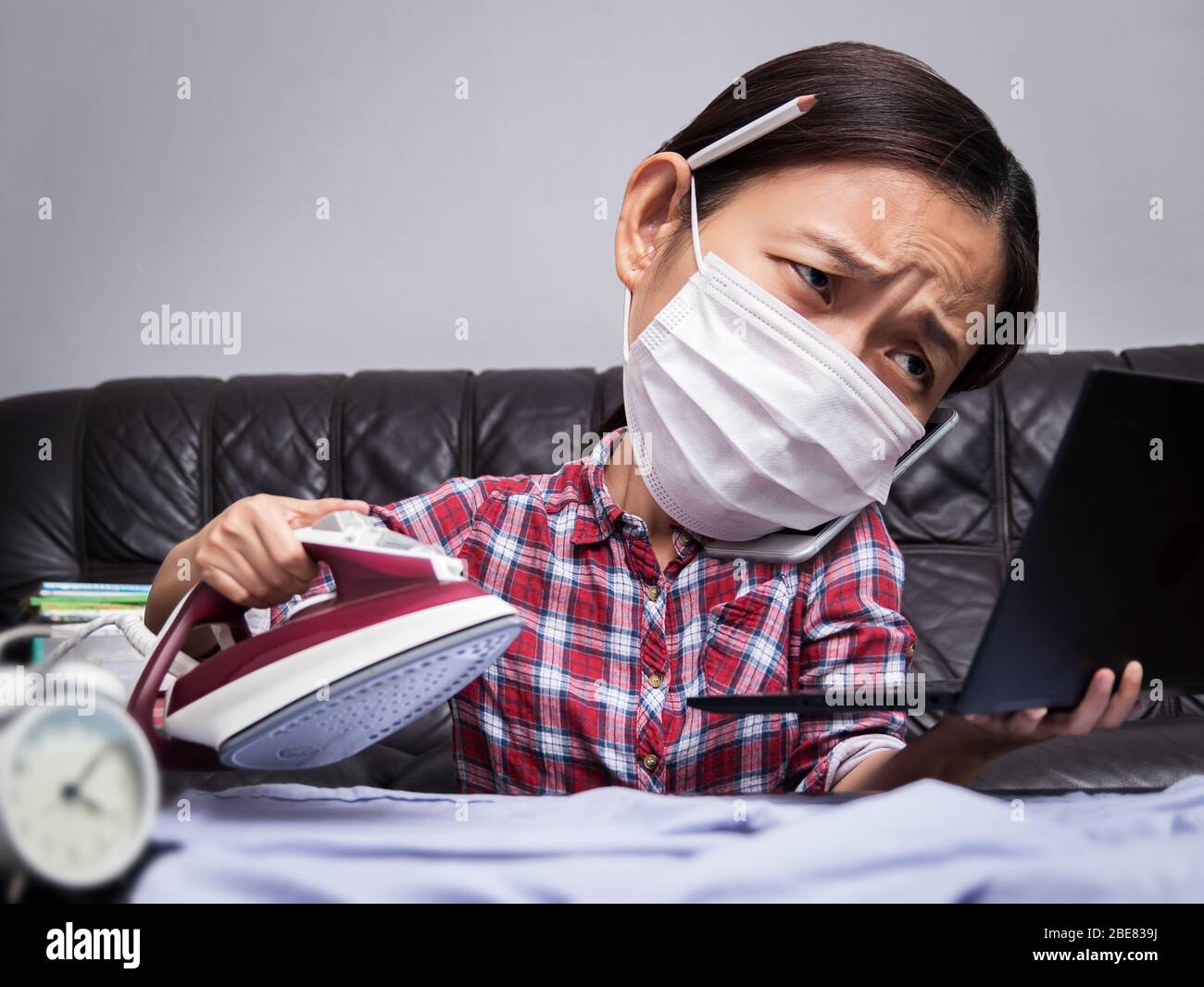 donna che lavora con parti di lavoro e di casa molto occupate, stirare i panni, parlare al telefono e lavorare con il computer portatile durante l'isolamento per evitare la sprea Foto Stock
