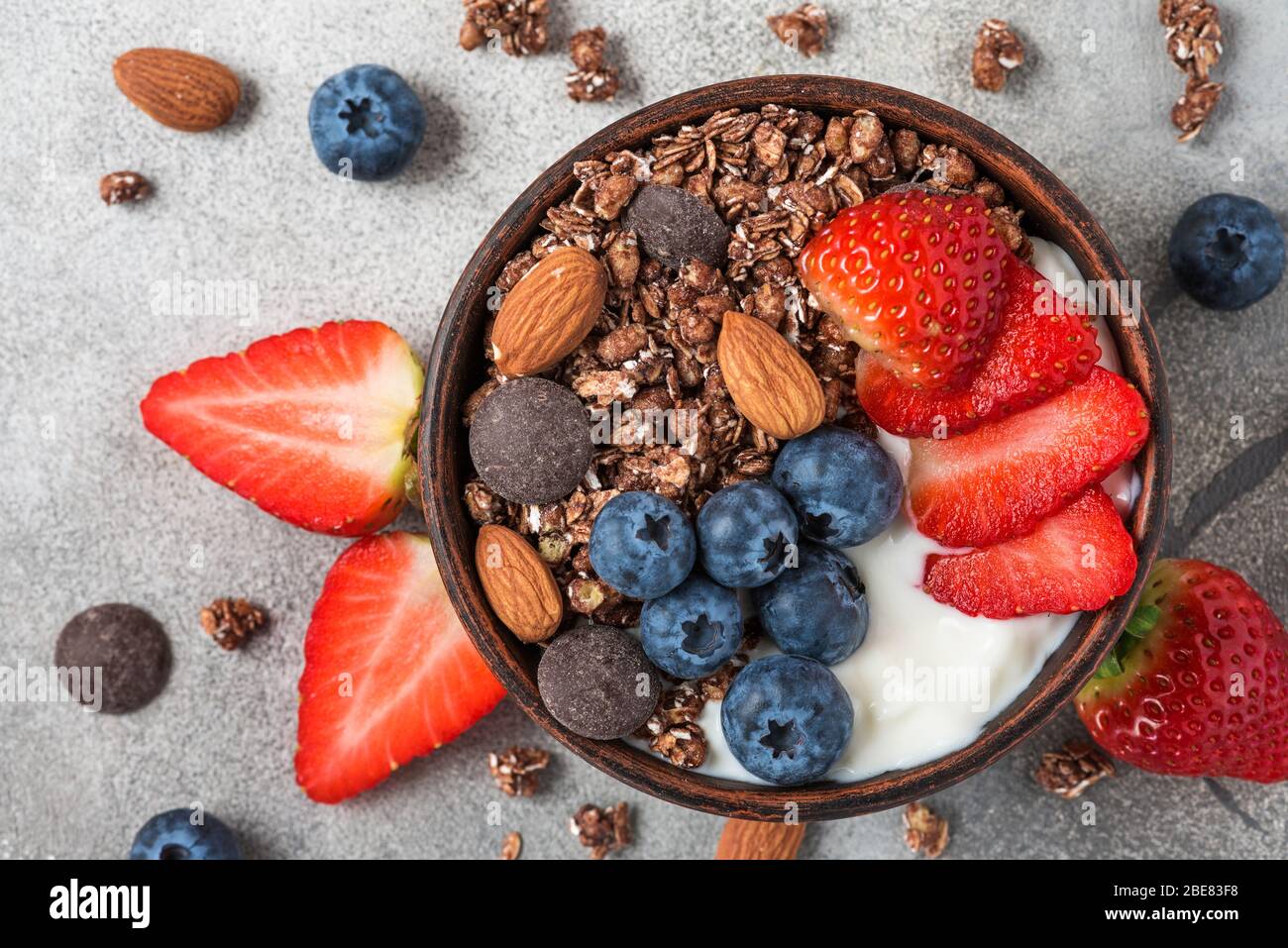Colazione sana con dieta, ciotola di cioccolato all'avena con yogurt, frutti di bosco freschi e mandorle sul tavolo grigio. Vista dall'alto Foto Stock