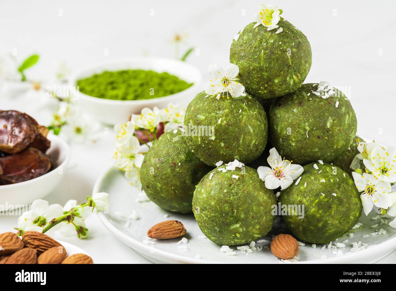 Palle di energia cruda fatte in casa fatte di tè matcha verde, datteri e noci con fiori di primavera. Sano cibo vegano dessert su sfondo bianco. Stile del cibo. Foto Stock
