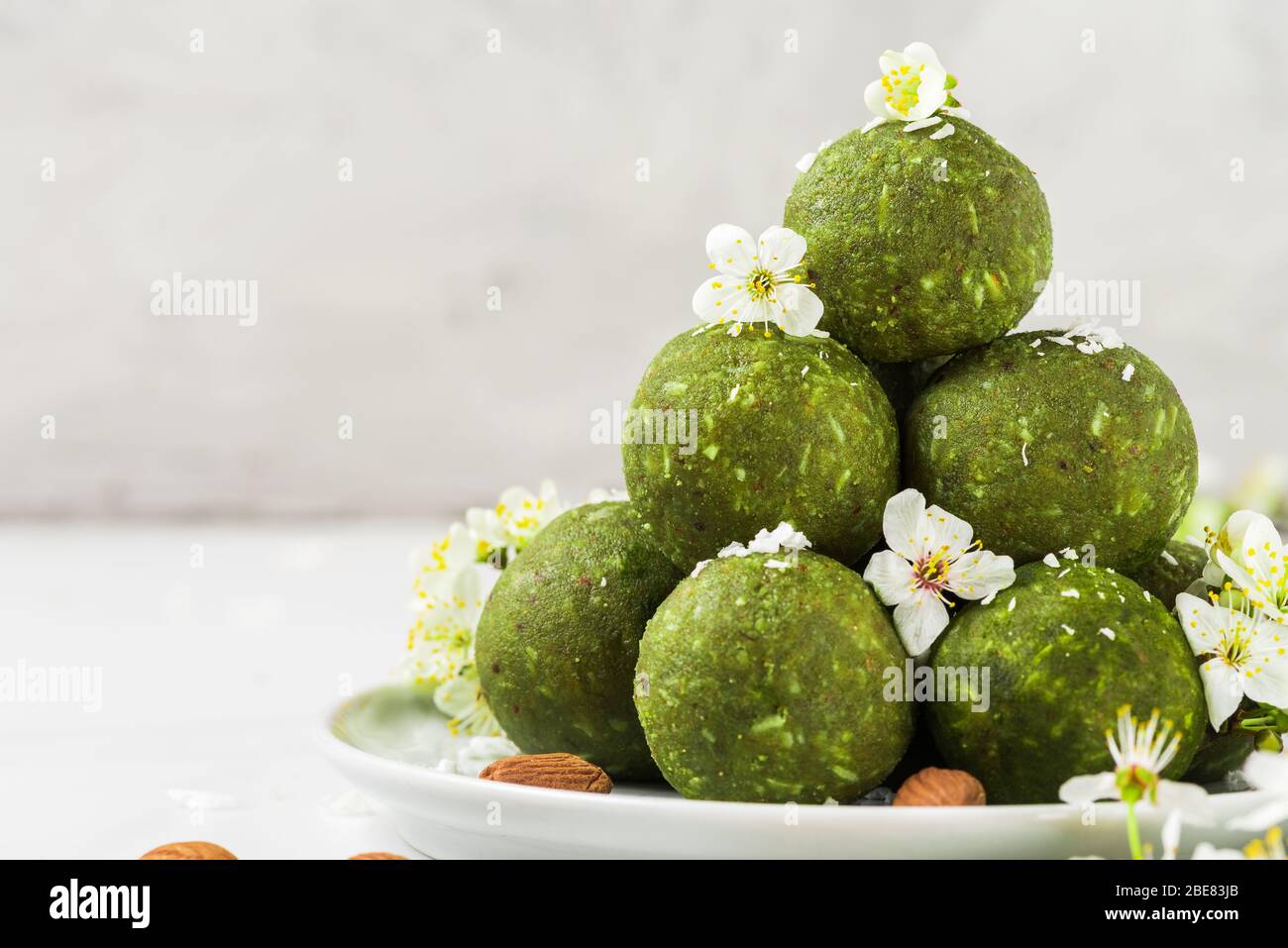 Sfere di energia vegana crude fatte di tè matcha, datteri e noci con fiori primaverili. Stile del cibo. Dessert vegano sano. Primo piano con spazio per le copie Foto Stock