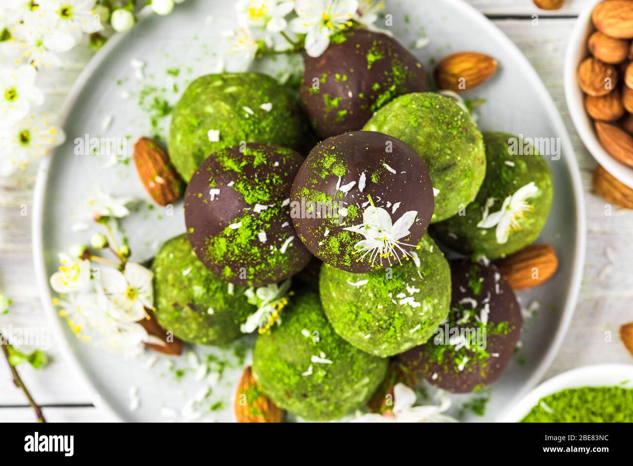 Dessert crudo di vegan verde matcha con palle di energia matcha in glassa di cioccolato e fiori primaverili. Vista dall'alto. Dessert vegano sano Foto Stock