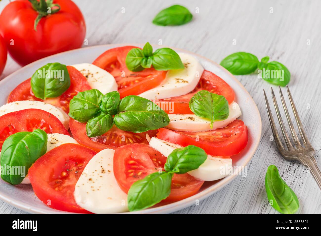 Insalata caprese con pomodori maturi e mozzarella con foglie di basilico fresco in un piatto con forchetta. Cucina italiana, vista dall'alto Foto Stock