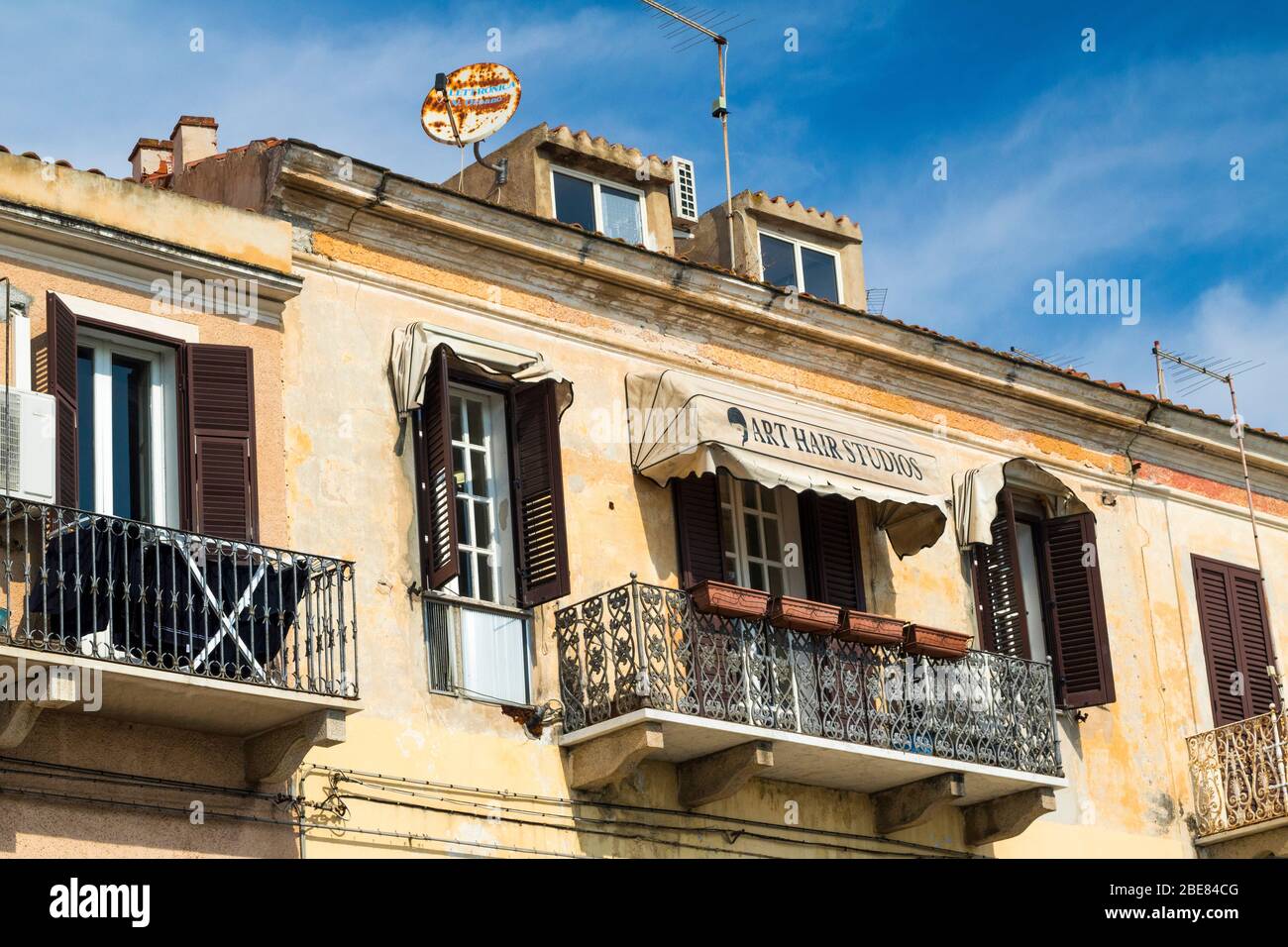 Balconi e persiane: Immagine esterna dettagliata di un parrucchiere al piano superiore con persiane Louvered su un edificio nella strada principale di la Maddalena Foto Stock