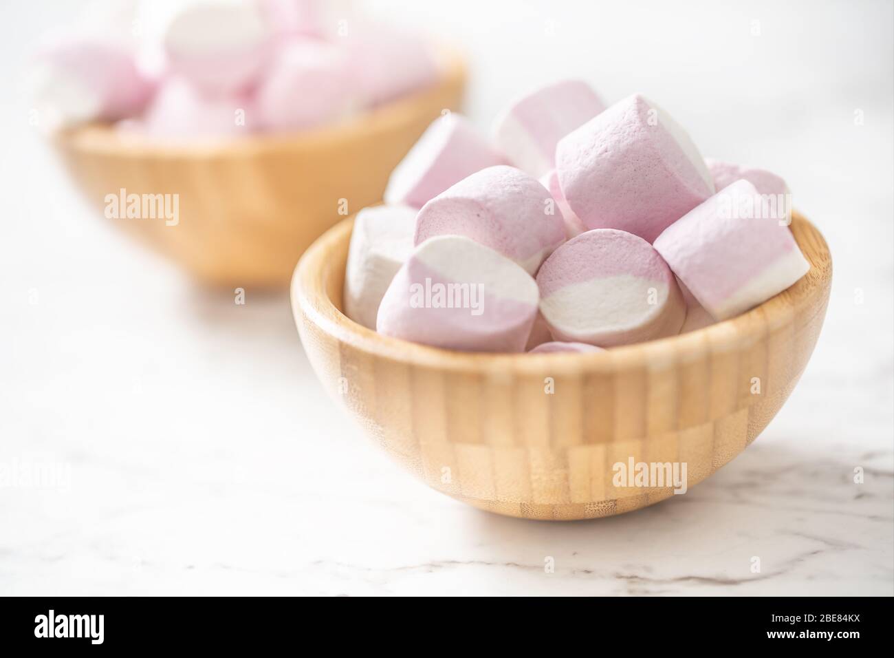 Marshmallow rosa e bianco in tini di legno posti su una superficie di marmo con un fuoco sulla ciotola nella parte anteriore. Foto Stock