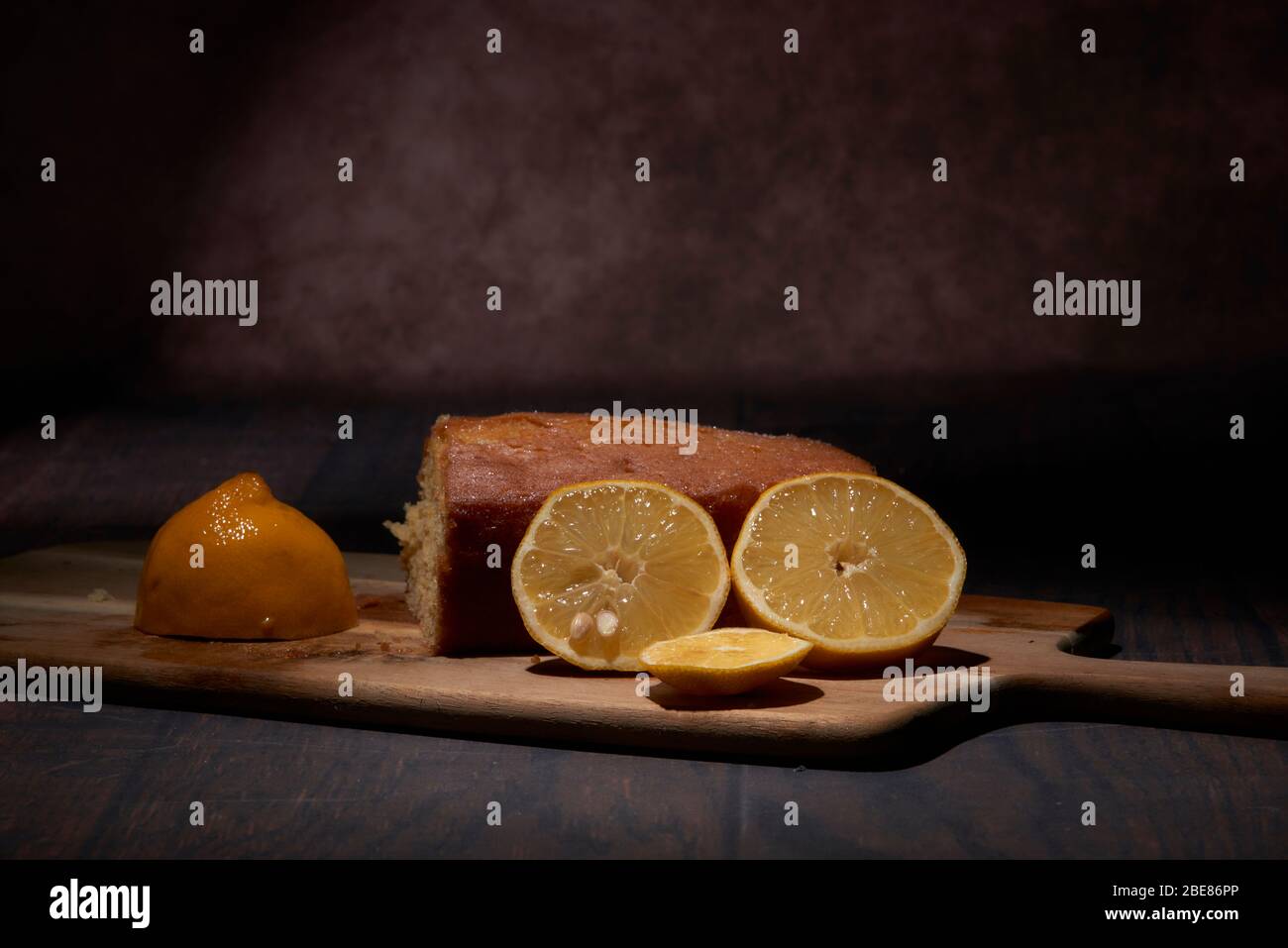 Torta al limone fatta in casa con limoni freschi su un pannello di legno in studio allestito. Illuminazione studio con sfondo scuro e spazio copia Foto Stock