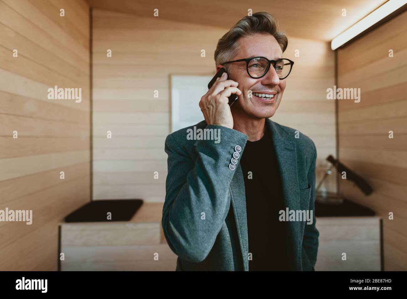 Uomo d'affari maturo che parla al telefono. Imprenditore maschio sicuro in piedi in ufficio facendo una chiamata. Foto Stock