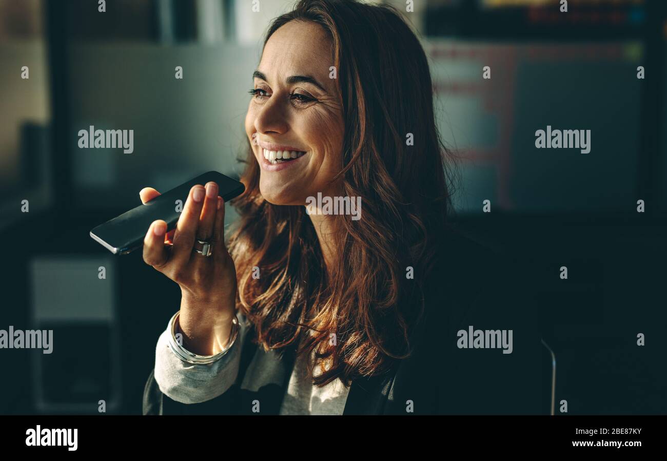 Imprenditore che parla al telefono con altoparlante e sorridente. Dirigente femminile che parla al telefono cellulare in ufficio. Foto Stock