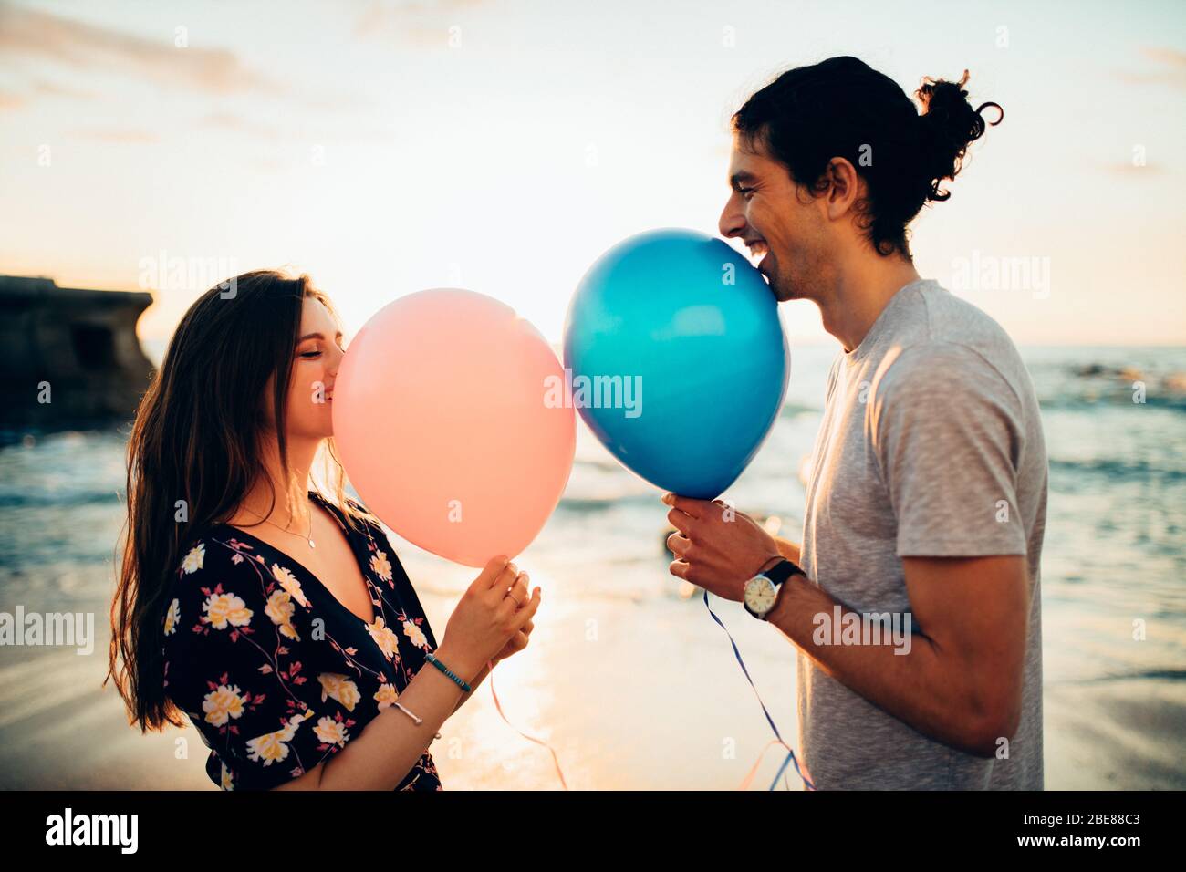 Coppia in piedi data all'aperto in spiaggia con mongolfiera. Giovane uomo e donna con palloncini sorridenti in spiaggia. Foto Stock