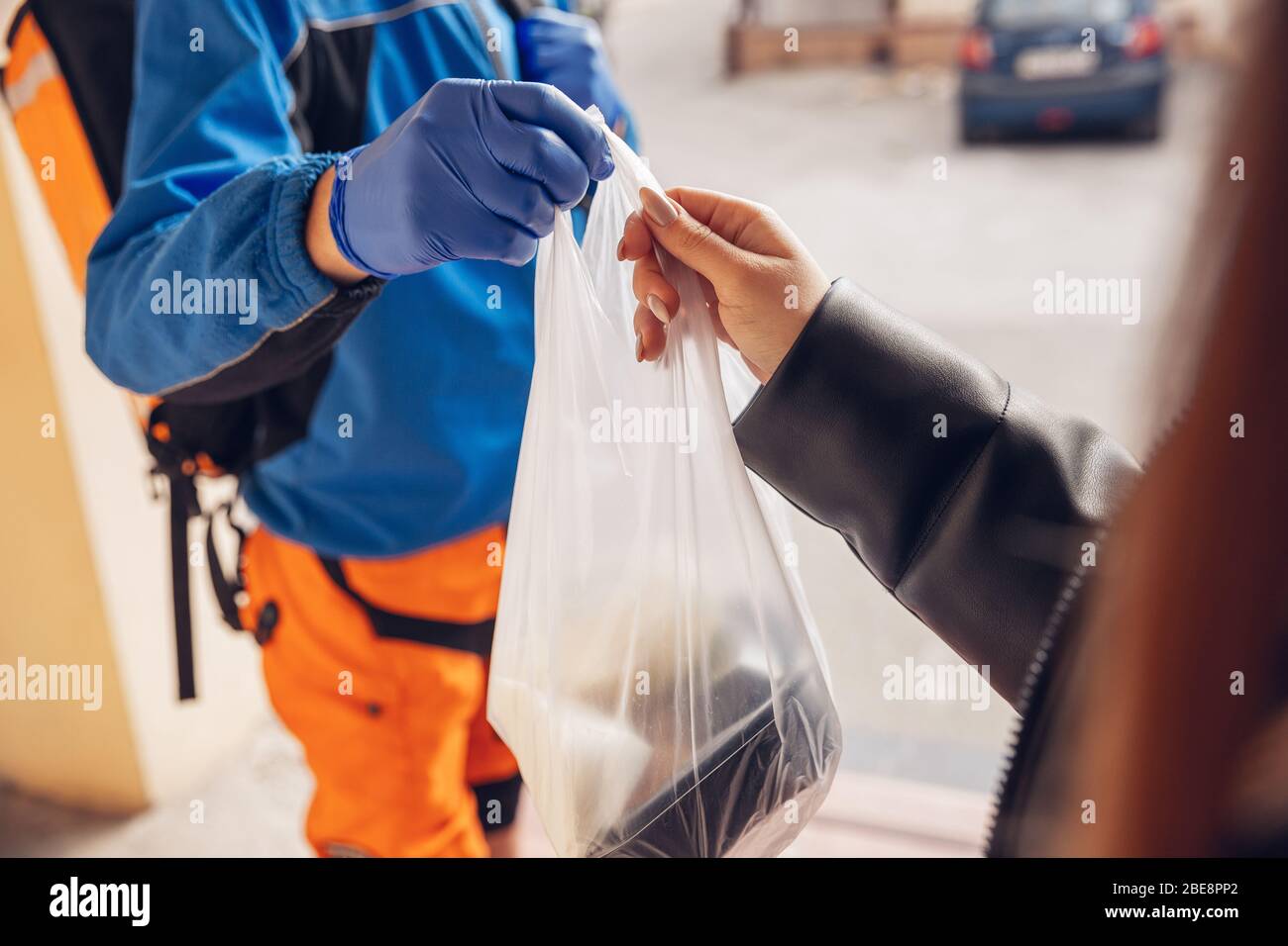 Servizio di consegna senza contatto durante la quarantena. L'uomo consegna cibo e borse per la spesa durante l'isolamento. Bussando alla porta e lascia le merci fino a quando il cliente non la prende. Sicurezza, ricezione, mantenimento della distanza. Foto Stock