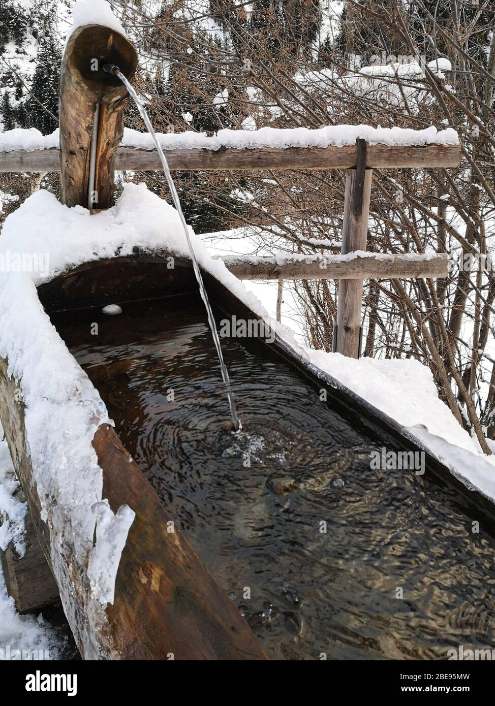 Fontana di montagna fatta di un tronco di legno scavato all'interno coperto di neve in inverno. Foto Stock