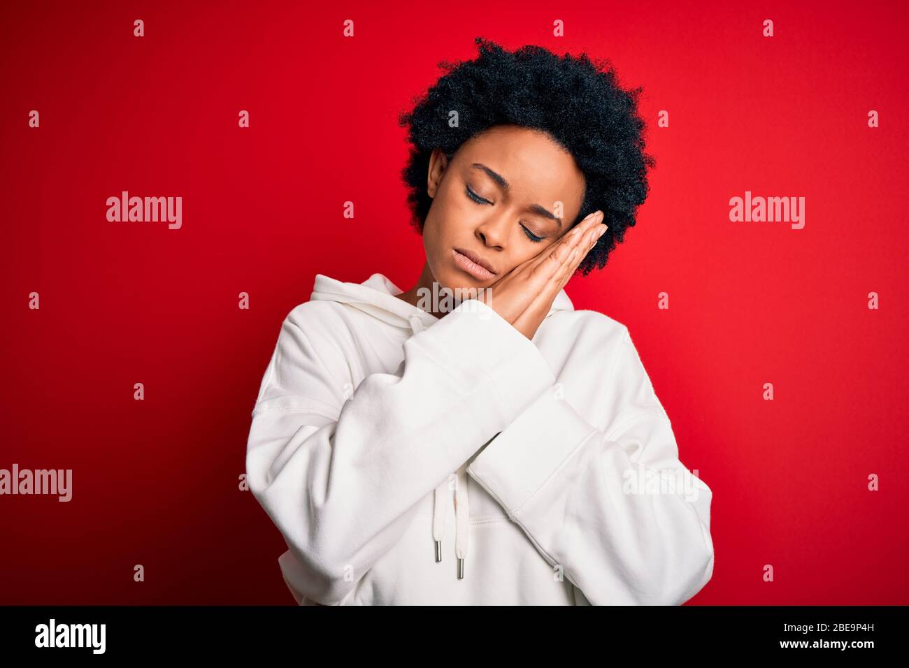 Giovane bella Afro americano sportivo con capelli ricci indossare abbigliamento sportivo dormire stanco sognare e posare con le mani insieme mentre sorridi Foto Stock