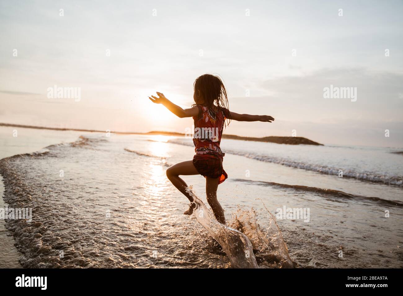 Una bambina asiatica che corre e salta sulla spiaggia mentre gioca sull'acqua su una bella spiaggia Foto Stock