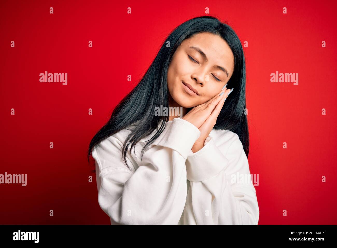 Giovane bella donna cinese sportivo indossare felpa su sfondo isolato rosso dormire stanco sognare e posare con le mani insieme mentre sorridono Foto Stock