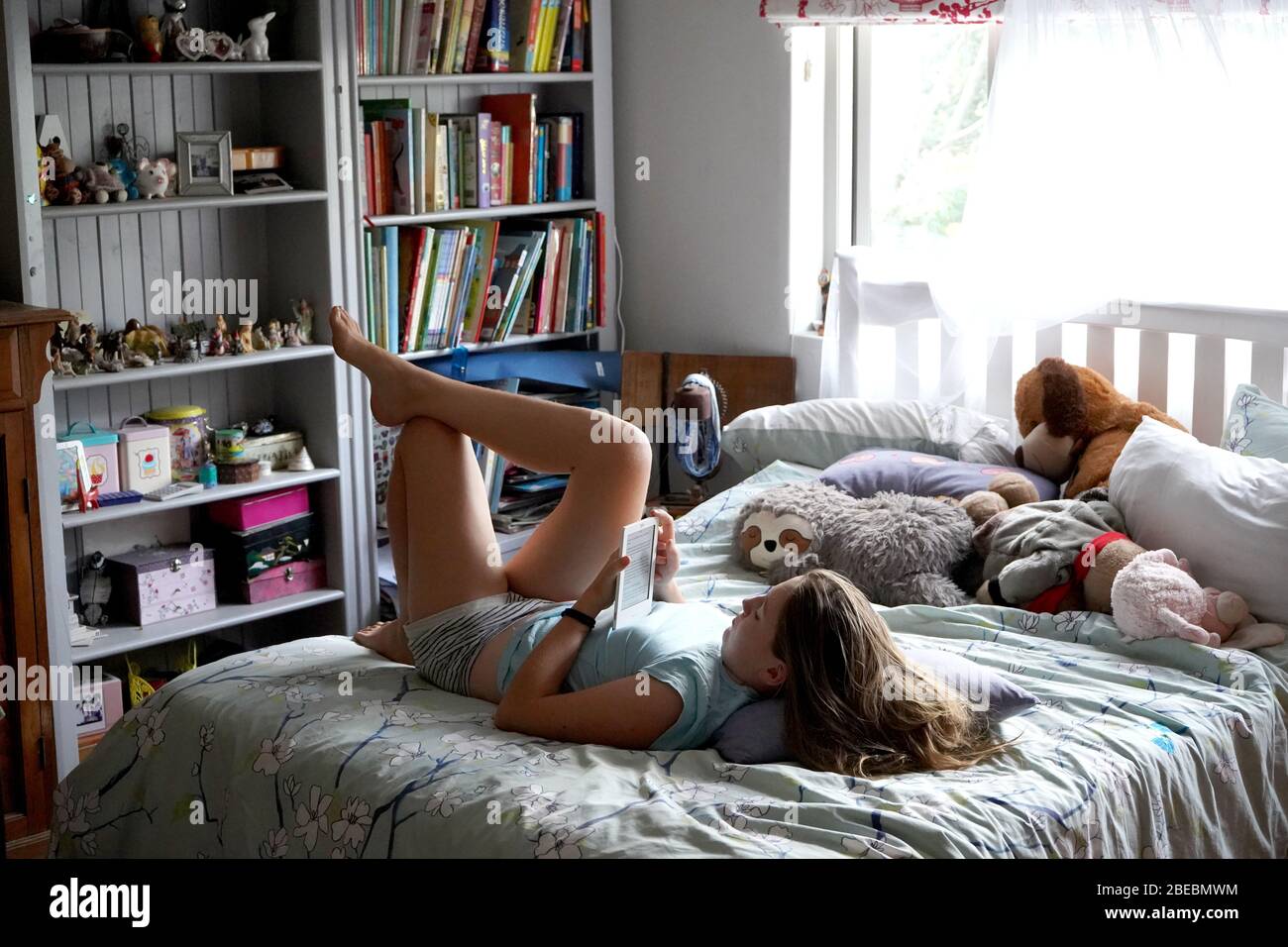 Giovane ragazza che legge un e-reader sul suo letto nella sua camera da letto Foto Stock