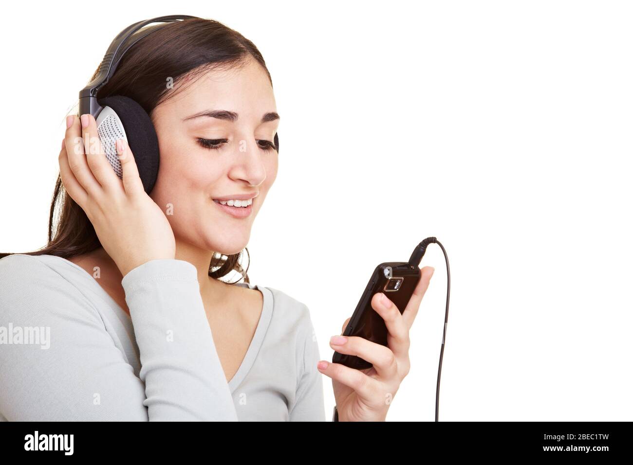 Donna giovane ridente con telefono cellulare guarda i video online con le cuffie Foto Stock