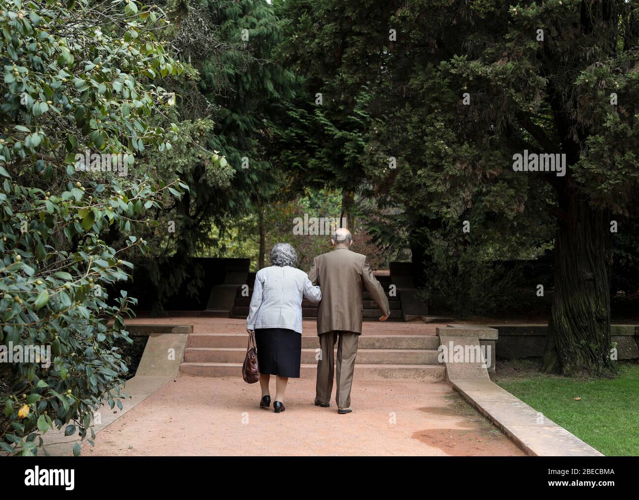 Una vecchia coppia ben vestita camminare romanticamente braccio in braccio nel parco. Foto Stock