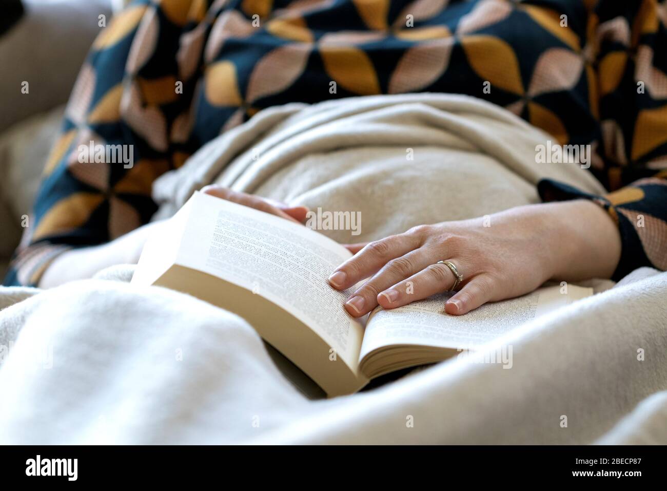 Un ritratto di una persona addormentata sotto una coperta mentre legge un libro. La mano della persona è ancora sul libro al punto in cui ha dozed fuori Foto Stock