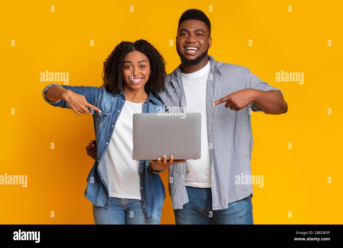 Allegra coppia nera che tiene in mano il laptop e lo indica Foto Stock